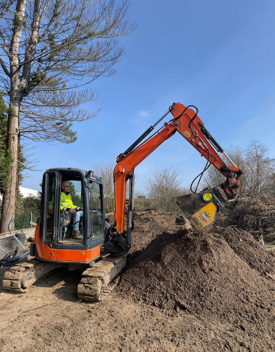 Facharbeiter bedient einen orangefarbenen Minibagger bei Erdarbeiten auf einer privaten Baustelle im Garten